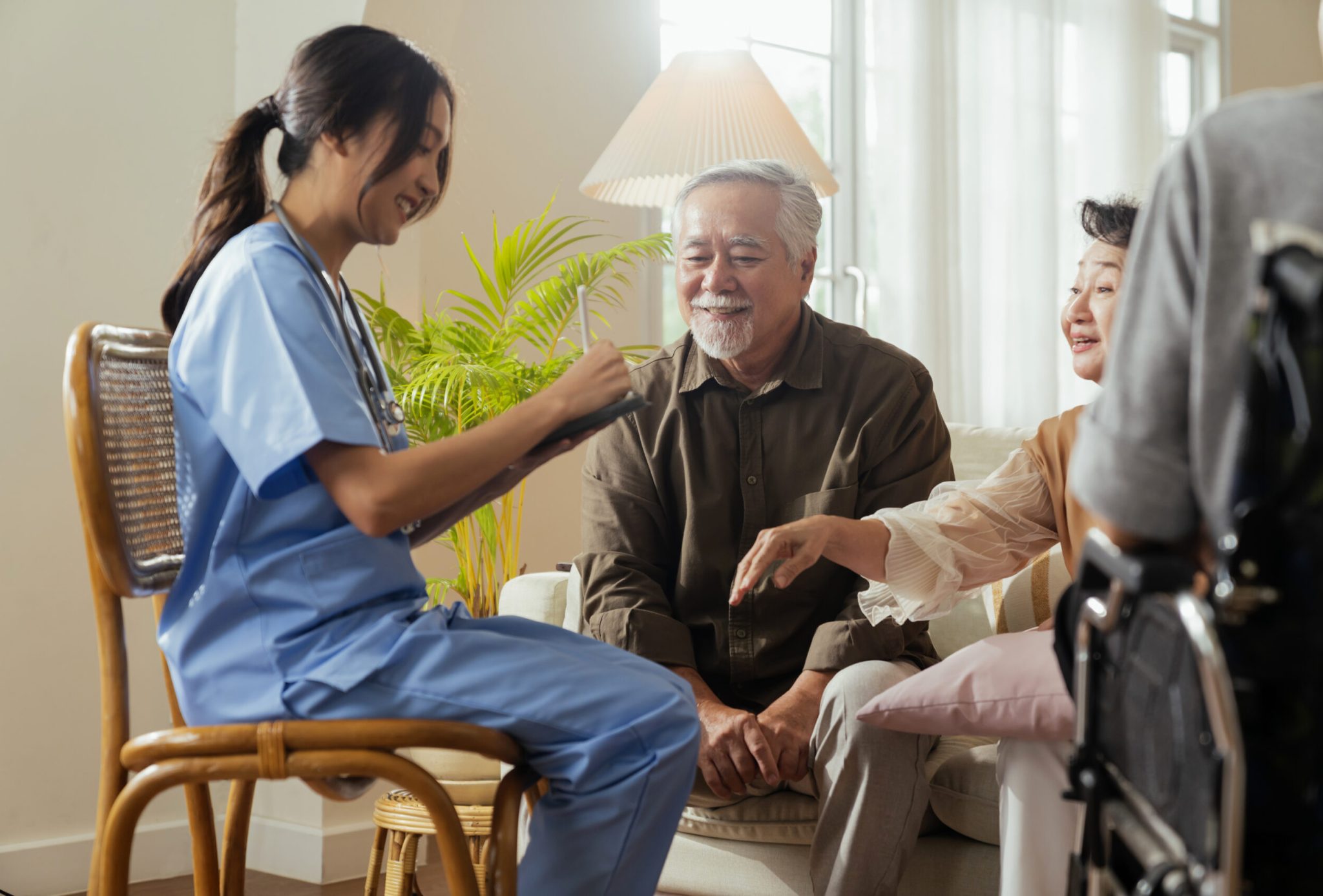 happiness Cheerful elderly woman and men talking with female caregiver nurse doctor having health checking consult at living area,Caretakers with senior couple sitting in living room at nursing home